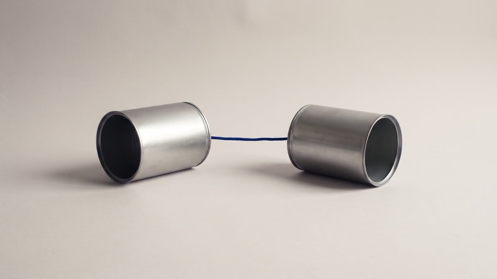 A tin-can telephone: two plain tin cans joined base to base by one taut blue string