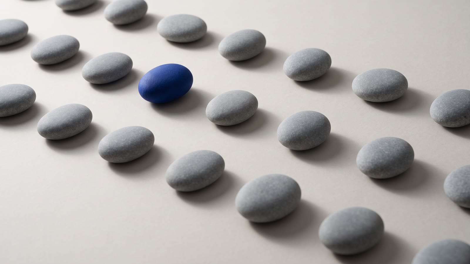 Rows of identical grey pebbles with one blue pebble